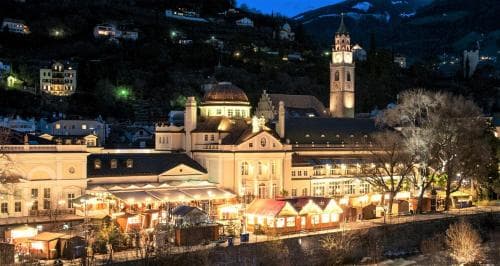 A charming nighttime view of a historic town square illuminated by festive lights, featuring a prominent clock tower and cozy market stalls, evokes a warm and inviting atmosphere perfect for winter travel and cultural exploration.