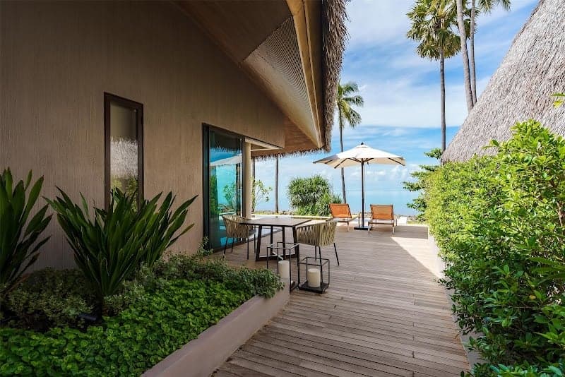 A serene tropical villa deck at Hyatt Regency Koh Samui features lush greenery, comfortable seating under an umbrella, and a stunning ocean view, ideal for travelers seeking relaxation and luxury in Thailand.