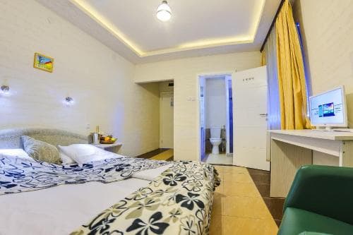 A cozy hotel room features a neatly made bed with floral bedding, a desk with a computer, warm lighting, and an open bathroom door, ideal for travelers seeking comfort and convenience.