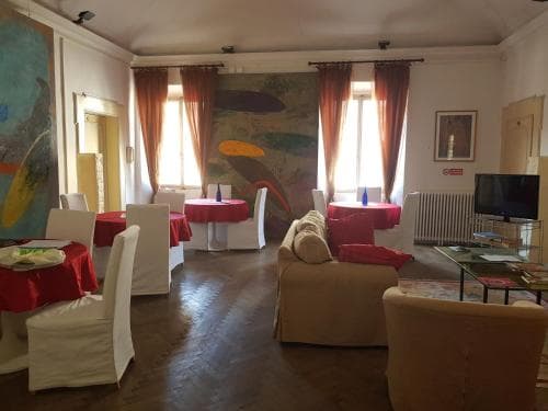 A cozy, warmly lit dining area with wooden floors, red-clothed tables, modern art on the walls, and comfortable seating creates an inviting atmosphere perfect for travelers seeking a relaxed meal or gathering space.