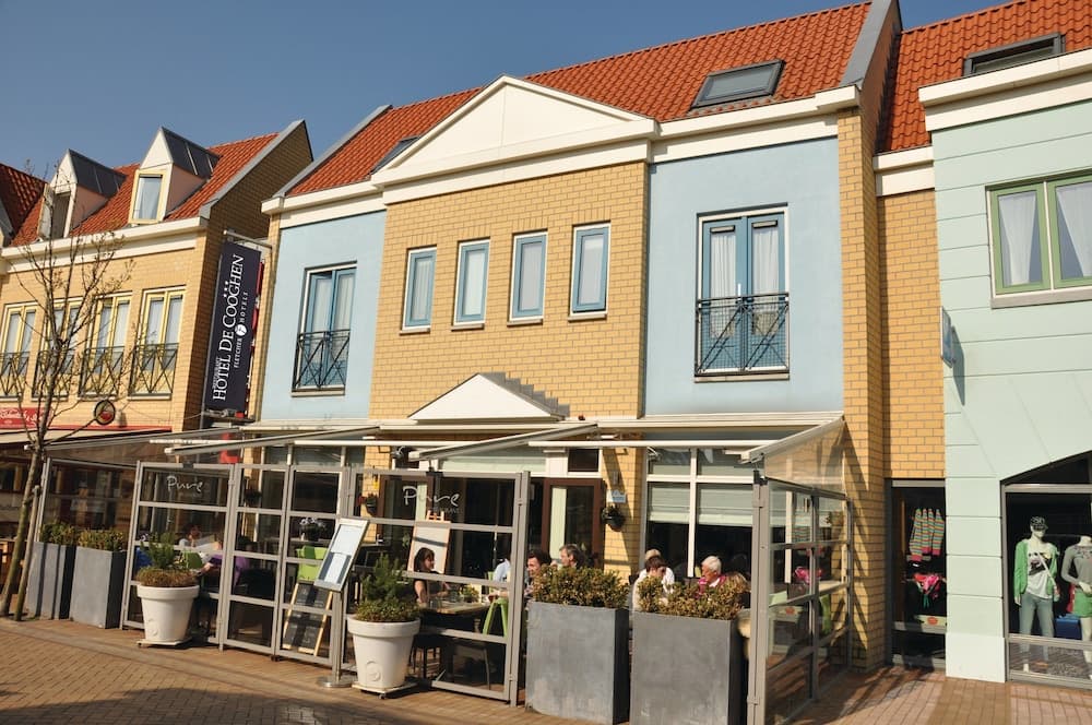 A charming European-style shopping street features pastel-colored buildings with outdoor seating under clear skies, ideal for leisurely strolls and dining experiences.