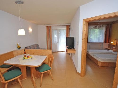 A cozy apartment interior featuring a dining area with a wooden table set for breakfast, a small TV on a stand, and an open doorway leading to a bedroom, ideal for travelers seeking comfortable and functional accommodation.