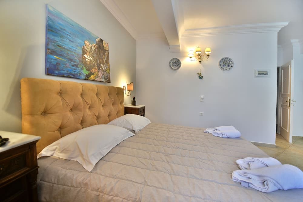 A cozy hotel room features a plush bed with a mustard tufted headboard, vibrant wall art, elegant sconces, and neatly folded towels, ideal for travelers seeking comfort and style.