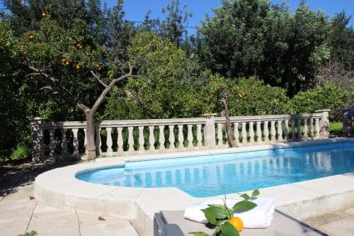 A serene outdoor pool surrounded by lush orange trees and a stone balustrade offers a tranquil retreat, perfect for a relaxing vacation getaway.
