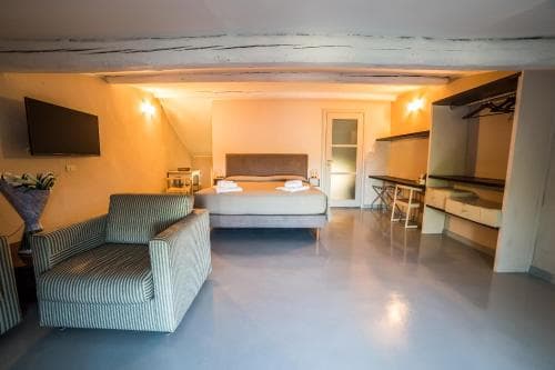 A cozy studio apartment features a modern bed, striped sofa, and sleek kitchenette under exposed beams, creating an inviting atmosphere ideal for travelers seeking comfort and style in a compact space.