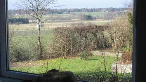 A serene rural landscape framed by a window showcases lush green fields, scattered trees, and distant hills, evoking a peaceful countryside retreat ideal for relaxation and nature photography.