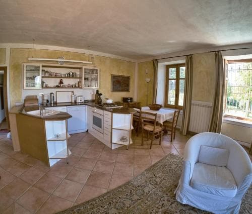 A cozy, sunlit kitchen-dining area with tiled floors, wooden furniture, and large windows offers a serene retreat ideal for travelers seeking a peaceful countryside rental experience.