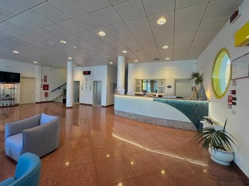A modern hotel lobby features sleek tiled floors, comfortable seating, a reception desk with a curved counter, and decorative plants, creating a welcoming atmosphere ideal for travelers seeking a professional yet cozy check-in experience.