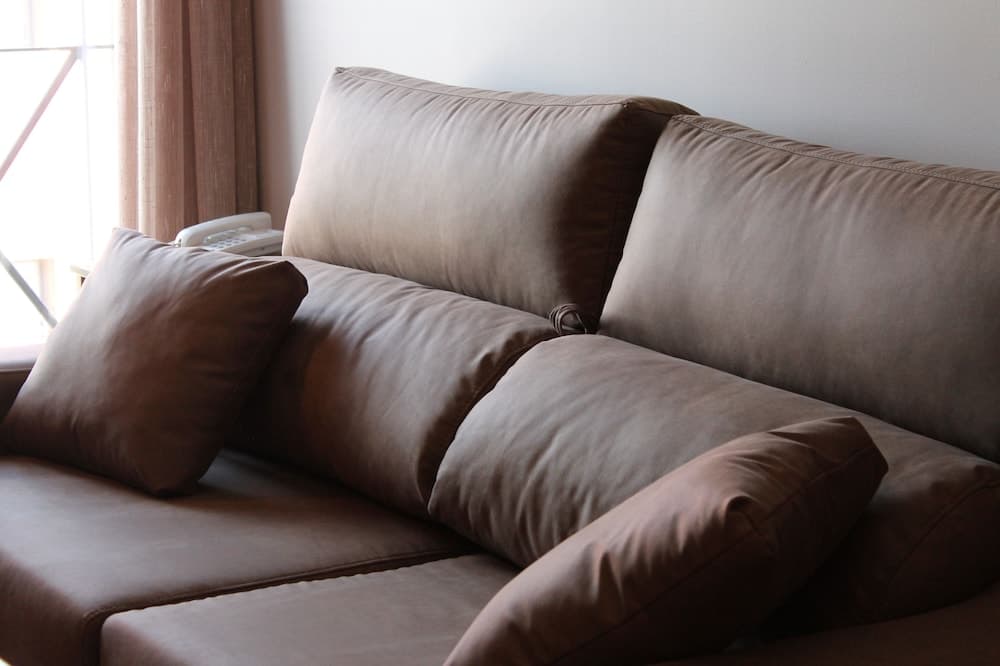 A cozy brown leather sofa adorned with plush cushions sits invitingly in a softly lit room near a window with curtains, ideal for travelers seeking comfort in a hotel suite or vacation rental.