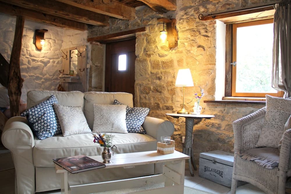 A cozy stone-walled cottage interior with rustic wooden beams, soft lighting, comfortable seating, and charming decor creates an inviting atmosphere perfect for a relaxing getaway.