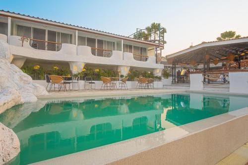 A serene hotel courtyard features a sparkling pool surrounded by lounge chairs and palm trees under a clear sky, ideal for a relaxing vacation getaway.