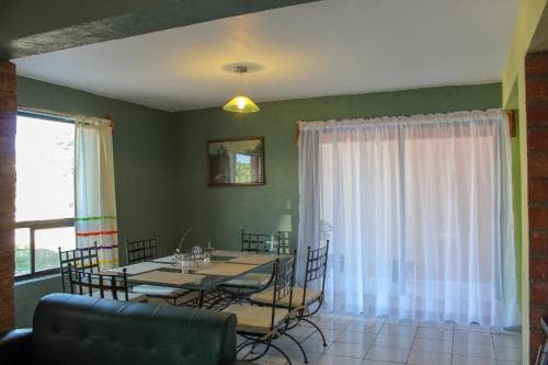 A cozy dining area with green walls, a glass table, metal chairs, and sheer curtains, ideal for travelers seeking a comfortable and inviting vacation rental space.