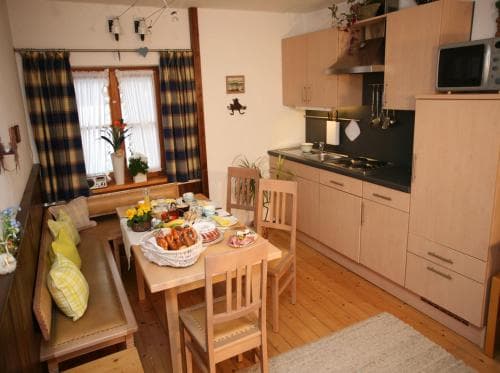 A cozy kitchen-dining area with wooden furniture, plaid curtains, and a well-set table invites travelers seeking a warm, homey retreat for a comfortable stay.