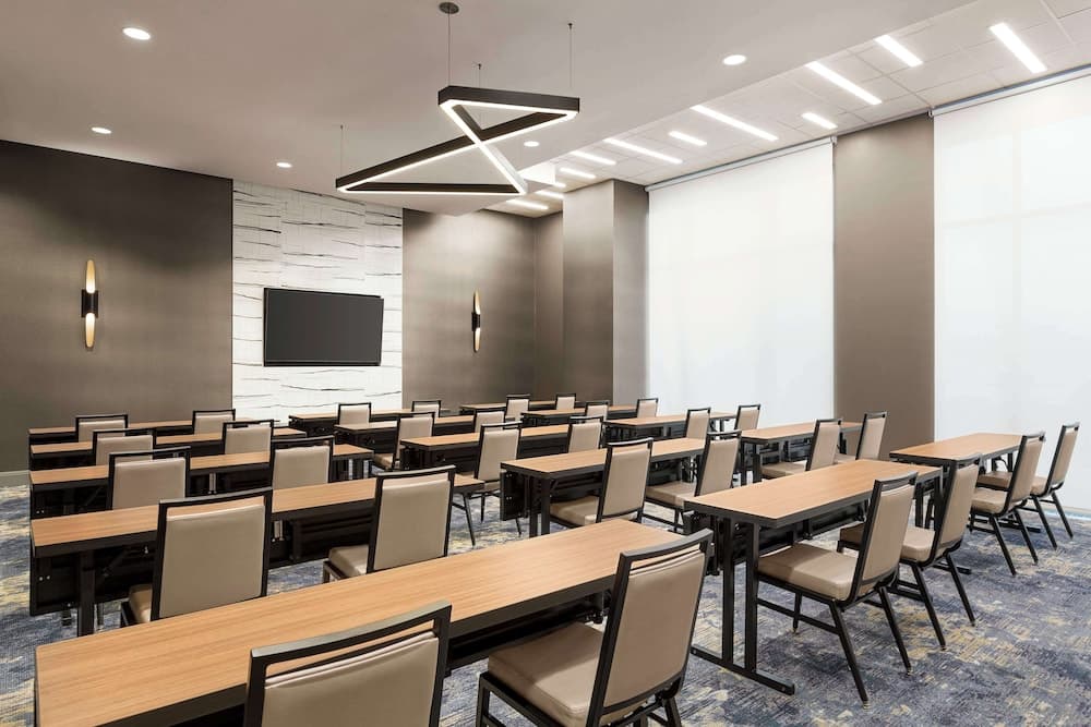 A modern conference room with rows of desks and chairs under geometric lighting fixtures, ideal for professional meetings and presentations.