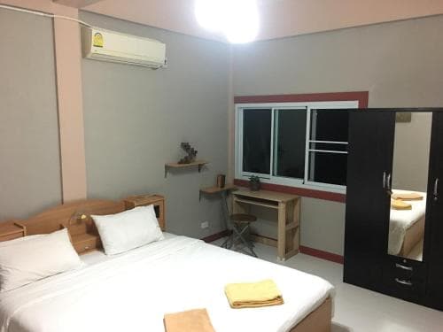A cozy hotel room features a neatly made bed, wooden desk, and mirror, set against soft gray walls with a window view, ideal for travelers seeking comfort and simplicity.