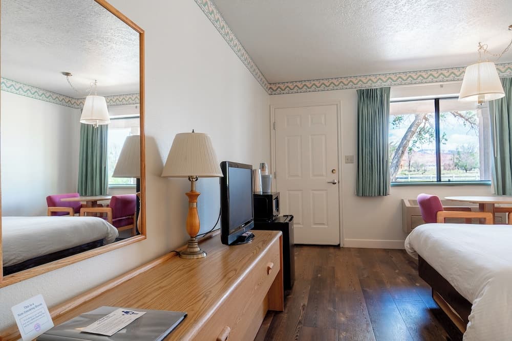 A cozy hotel room with wooden floors, twin beds, a desk with a lamp, and a scenic view through the window, ideal for travelers seeking comfort and relaxation.