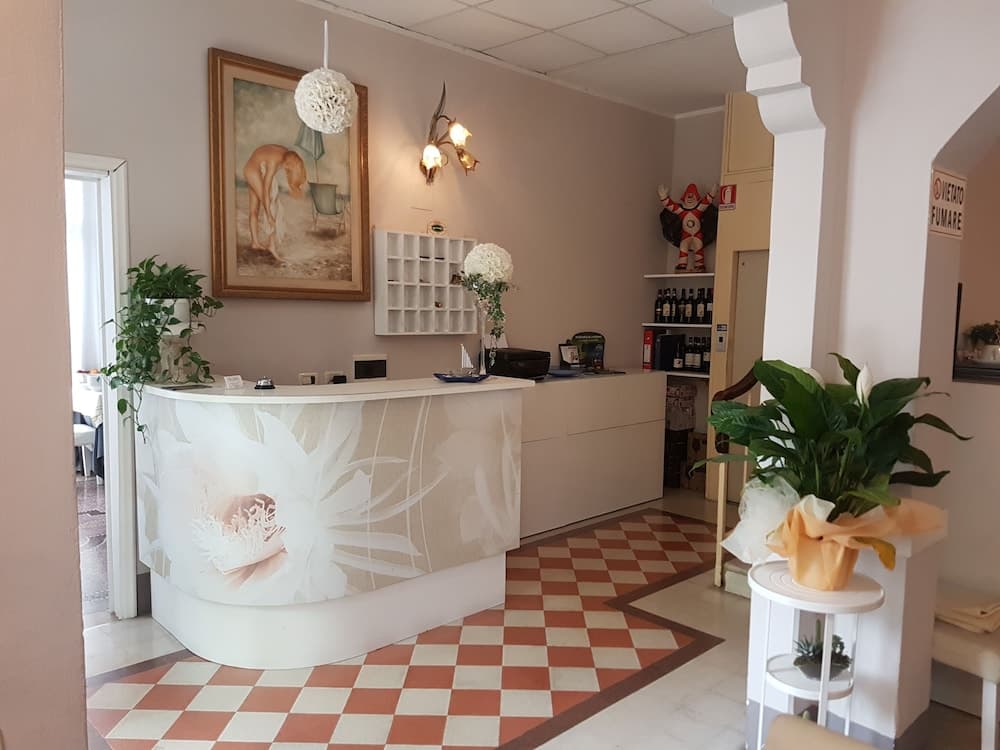 A cozy spa reception area features a floral-patterned desk, checkered flooring, decorative plants, and wall art, creating a welcoming atmosphere ideal for relaxation and wellness retreats.