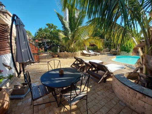 A serene tropical patio features a cozy seating area with a round table and chairs, surrounded by lush palm trees and a refreshing pool, ideal for a relaxing vacation getaway.