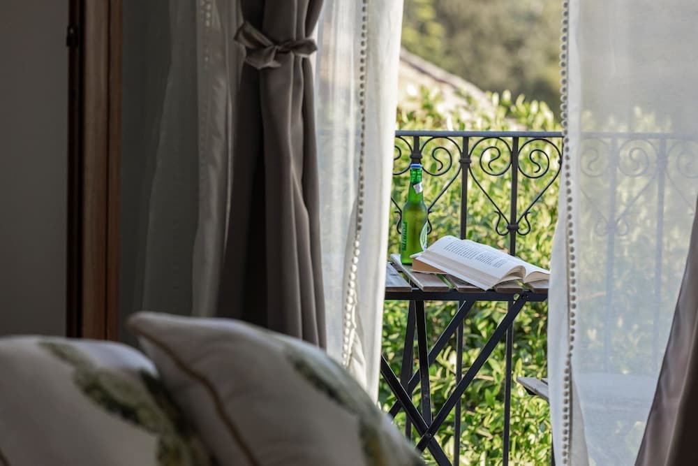 A serene balcony scene framed by sheer curtains, featuring a small table with an open book and a green bottle, evokes a tranquil retreat perfect for leisurely stays in a cozy vacation rental.