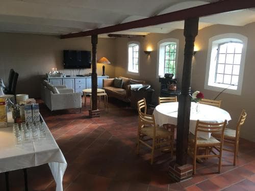 A cozy, rustic lounge area with exposed wooden beams, arched windows letting in natural light, comfortable seating, and a welcoming table setup creates an inviting atmosphere ideal for travelers seeking relaxation or small group gatherings.