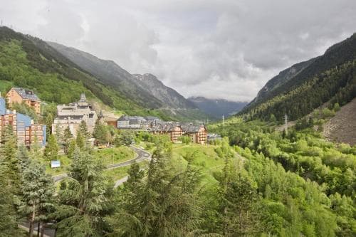 A serene mountain valley with lush greenery, quaint buildings nestled among the slopes, and a winding road invites travelers seeking a peaceful retreat in nature.