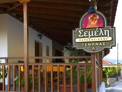 A cozy traditional taverna with wooden balconies and vibrant plants invites travelers to savor authentic Greek cuisine in a charming village setting.