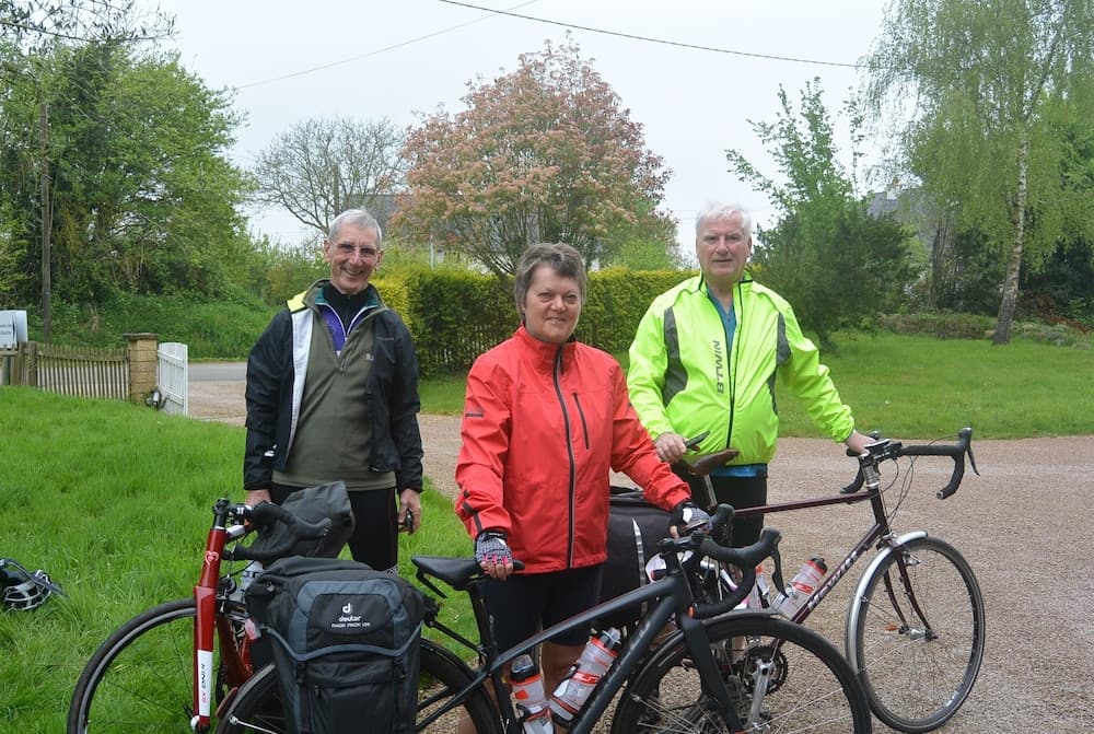 Three cyclists in vibrant jackets stand beside their bikes on a gravel path surrounded by lush greenery, creating an inviting scene for outdoor adventure enthusiasts.