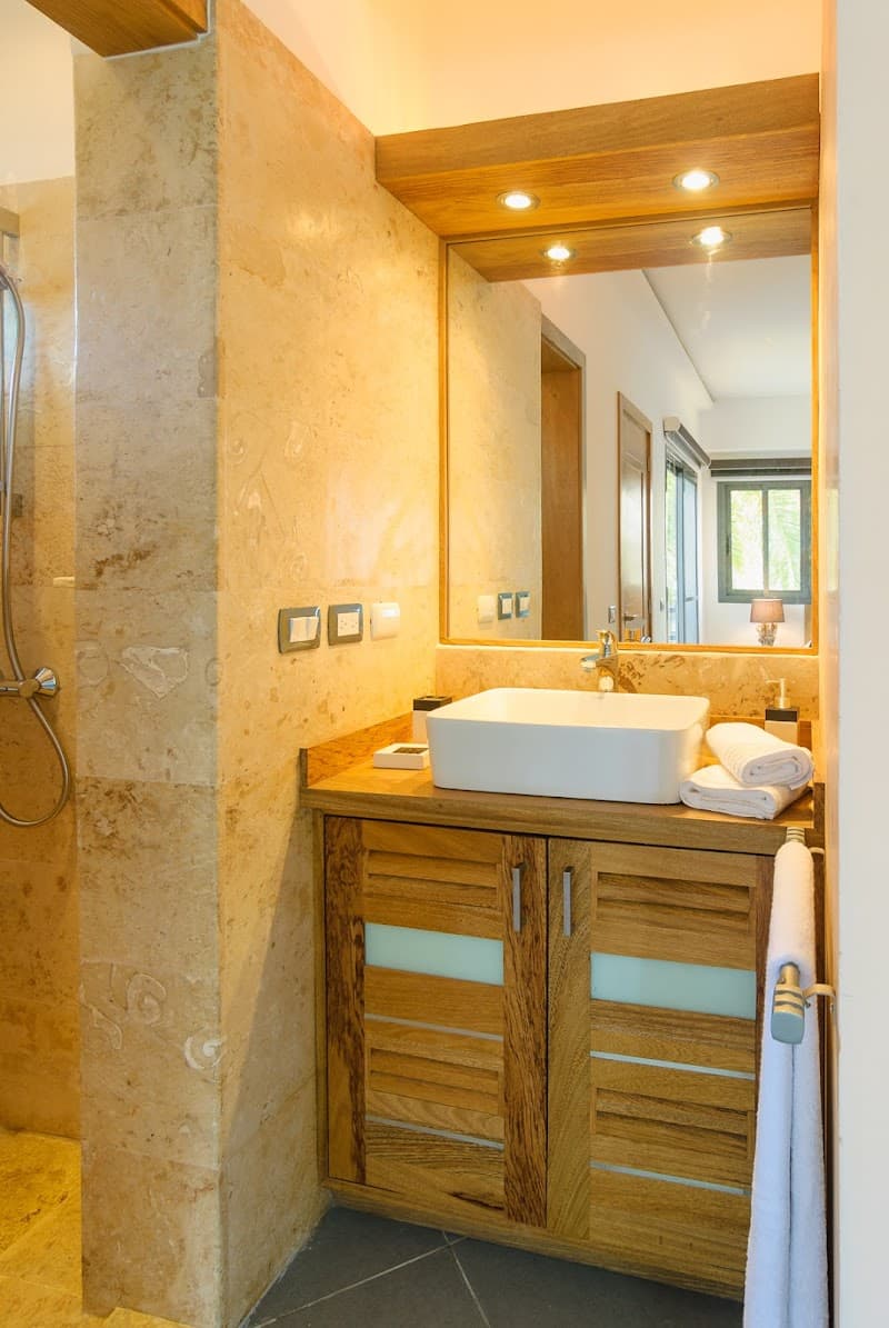 A cozy bathroom with warm lighting, wooden accents, and a modern sink setup invites travelers to unwind at the Aligio Playa Poppy in Las Terrenas, Dominican Republic.
