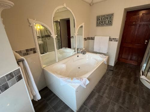 A cozy bathroom features a large white bathtub surrounded by tiled walls, arched mirrors, and a motivational quote, creating a serene retreat ideal for relaxation during a vacation stay.