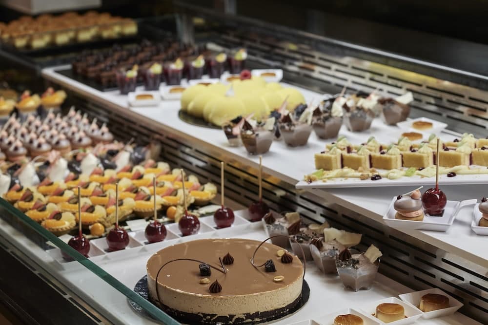 A vibrant bakery display showcases an array of decadent desserts like chocolate cakes, fruit-topped pastries, and caramel apples, creating an inviting atmosphere perfect for food enthusiasts exploring culinary delights.