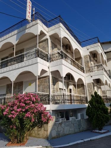A charming Mediterranean hotel with arched balconies and vibrant pink flowers invites travelers seeking a cozy seaside retreat.