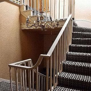 A warmly lit indoor staircase with patterned carpeting and elegant chandelier creates an inviting atmosphere, ideal for travelers seeking cozy accommodations in boutique hotels.
