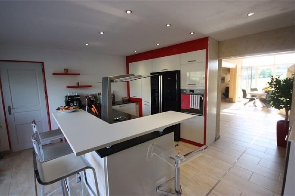 A modern kitchen with sleek white cabinets, red accents, and a central island invites travelers seeking a cozy yet stylish rental space for a homey getaway.
