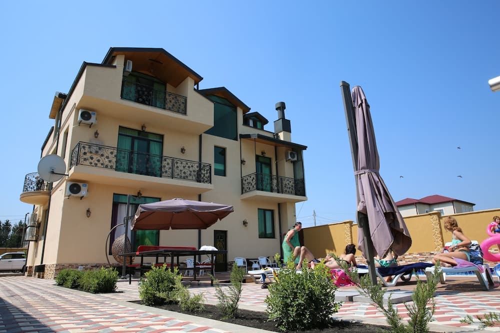 A sunny day at a cozy resort features guests relaxing under umbrellas near a charming multi-story building with balconies, ideal for leisure travelers seeking relaxation.