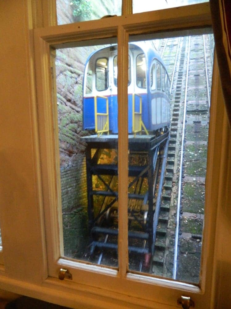 A quaint window view captures a charming blue funicular ascending a steep, mossy track, ideal for travelers exploring scenic urban transport systems.