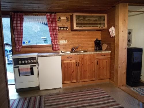 A cozy cabin kitchen with wooden cabinets, a stove, and a view of the outdoors through a window adorned with red curtains, ideal for travelers seeking a rustic retreat.