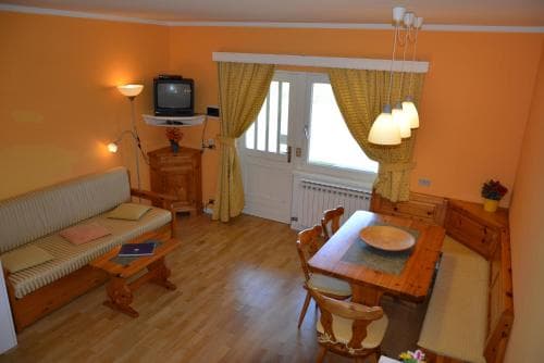A cozy living room with warm orange walls, wooden furniture, and a bright window creates an inviting atmosphere, perfect for travelers seeking a comfortable and homely accommodation.