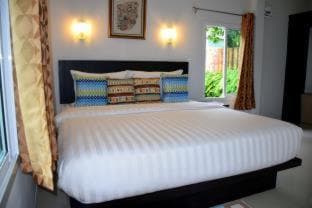 A cozy hotel room features a neatly made bed with colorful pillows, warm lighting, and a view of greenery through the window, ideal for travelers seeking comfort and relaxation.