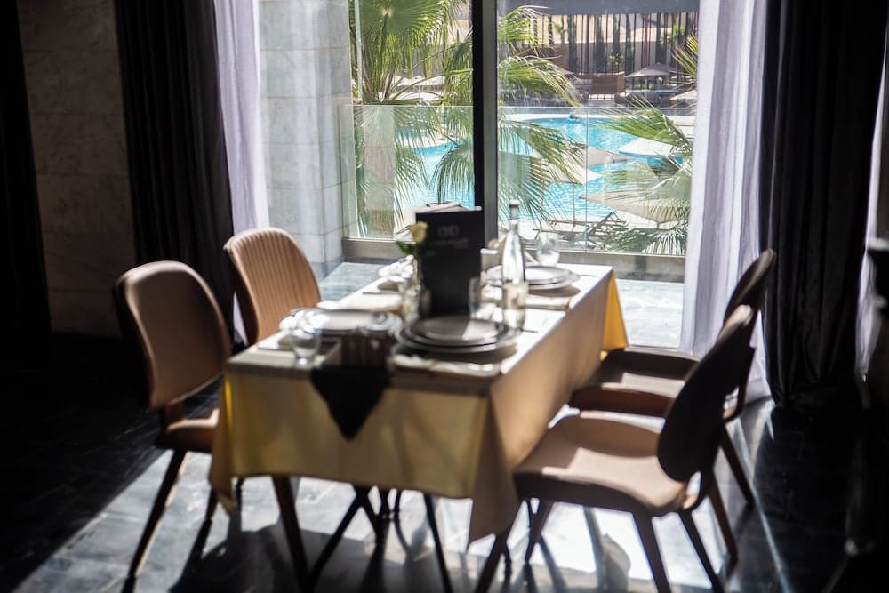 A cozy indoor dining setup with elegant tableware overlooks a serene poolside view through large windows, ideal for travelers seeking a luxurious and tranquil meal experience.