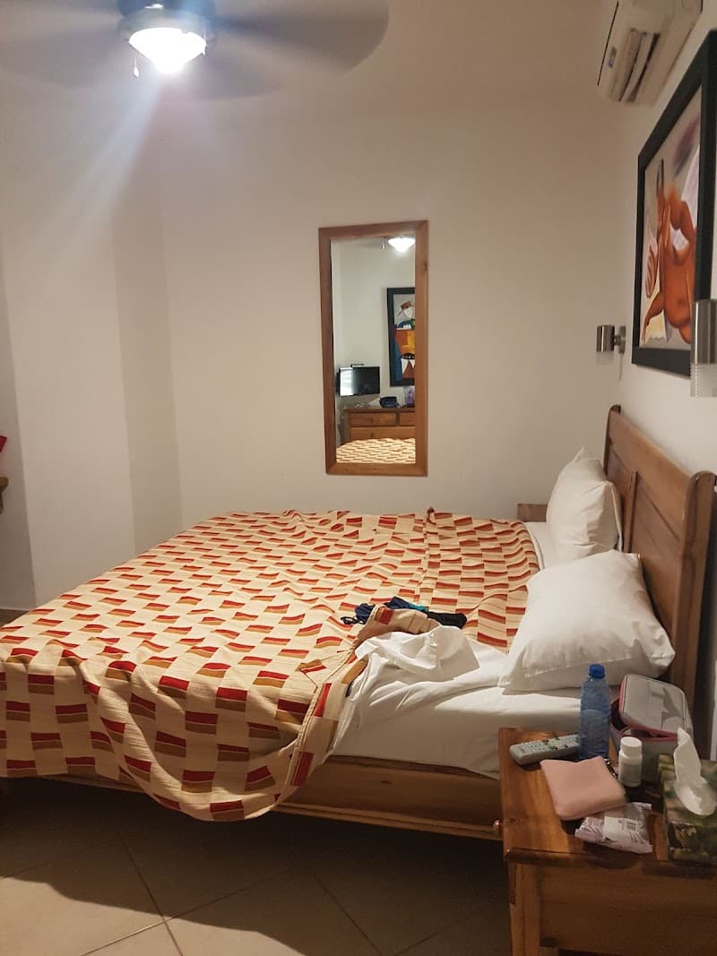 A cozy hotel room at Albachiara Beachfront Hotel in Las Terrenas, Dominican Republic, features a neatly made bed with patterned bedding, a wooden nightstand with personal items, and a mirror reflecting the warm ambiance, ideal for travelers seeking comfort near the beach.
