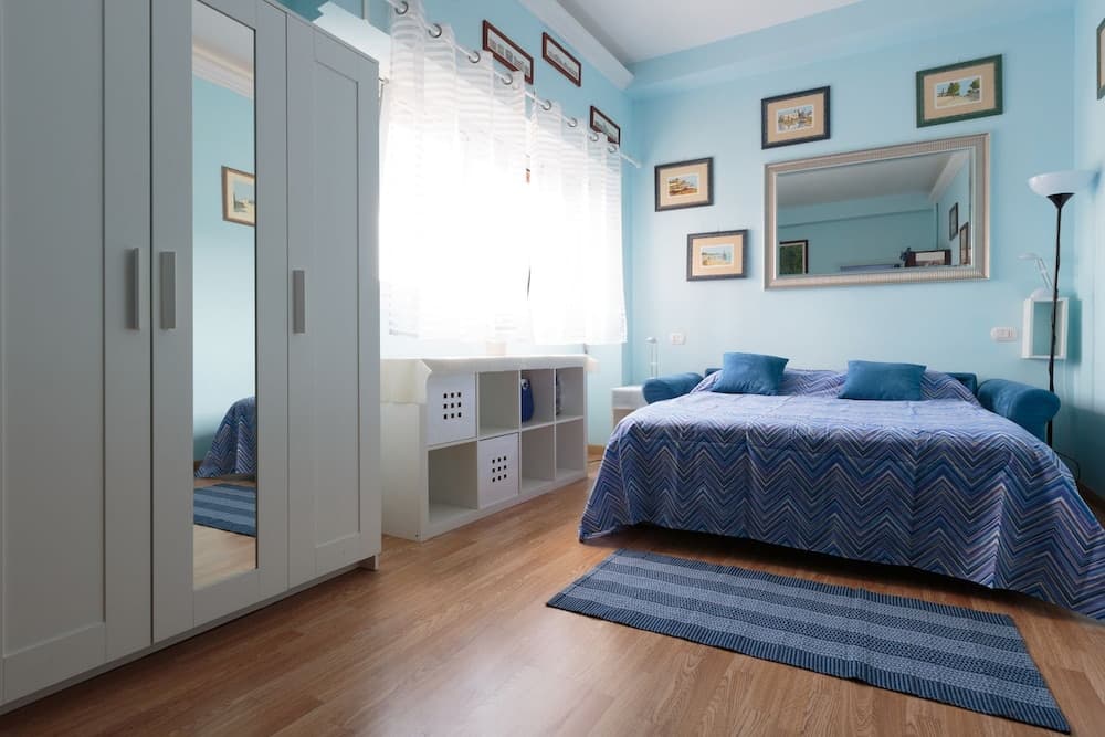 A serene bedroom with light blue walls, wooden flooring, and cozy blue bedding creates a tranquil atmosphere, ideal for travelers seeking a peaceful retreat.