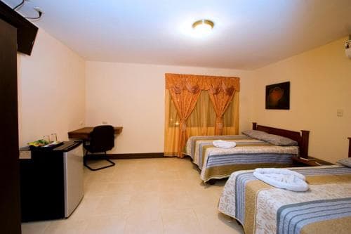 A cozy hotel room features two neatly made beds with striped linens, a desk with a chair, a small fridge, and warm-toned curtains over the window, ideal for travelers seeking comfort and convenience.