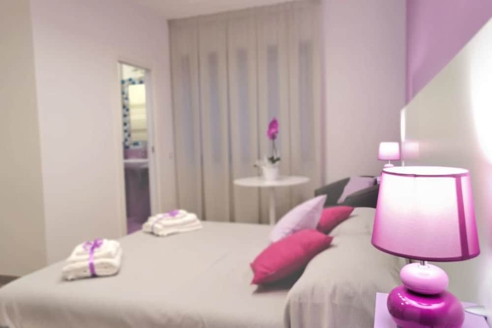A cozy bedroom with soft purple accents, neatly folded towels, and vibrant pillows creates a serene atmosphere ideal for travelers seeking relaxation and comfort.