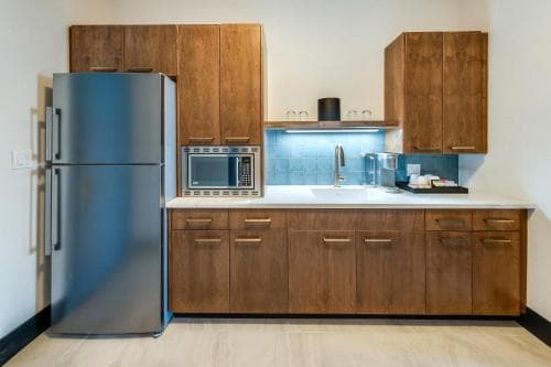 A modern kitchenette with wooden cabinets, stainless steel appliances, and a blue-tiled backsplash offers a cozy and functional space ideal for travelers seeking self-catering accommodations.