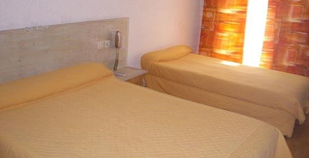A cozy hotel room features two neatly made beds with yellow linens, a bedside table with a phone, and warm-toned curtains, ideal for travelers seeking a comfortable and simple accommodation.