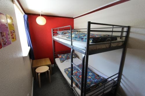A cozy hostel room with vibrant red walls, bunk beds adorned with colorful bedding, and simple furnishings creates an inviting atmosphere ideal for budget travelers seeking a comfortable stay.