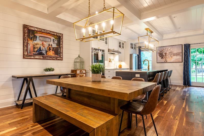 A cozy, rustic-chic dining area with wooden furniture, elegant gold chandeliers, and vibrant artwork creates a warm and inviting atmosphere perfect for travelers seeking a charming stay at the Barnstead Inn in Manchester Center, VT.