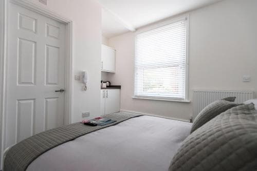 A cozy, minimalist bedroom with a neatly made bed, small kitchenette, and bright window with blinds, ideal for travelers seeking a clean and functional accommodation space.
