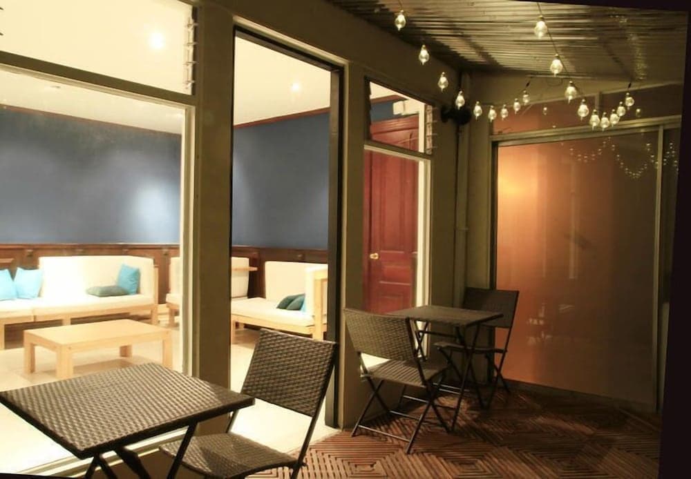 A cozy indoor-outdoor lounge area features modern furniture, string lights, and glass doors leading to a warmly lit interior, ideal for travelers seeking a relaxing retreat.