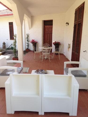 A cozy Mediterranean patio with terracotta flooring, white furniture, potted plants, and floral arrangements creates an inviting atmosphere ideal for relaxing stays at a charming vacation rental.